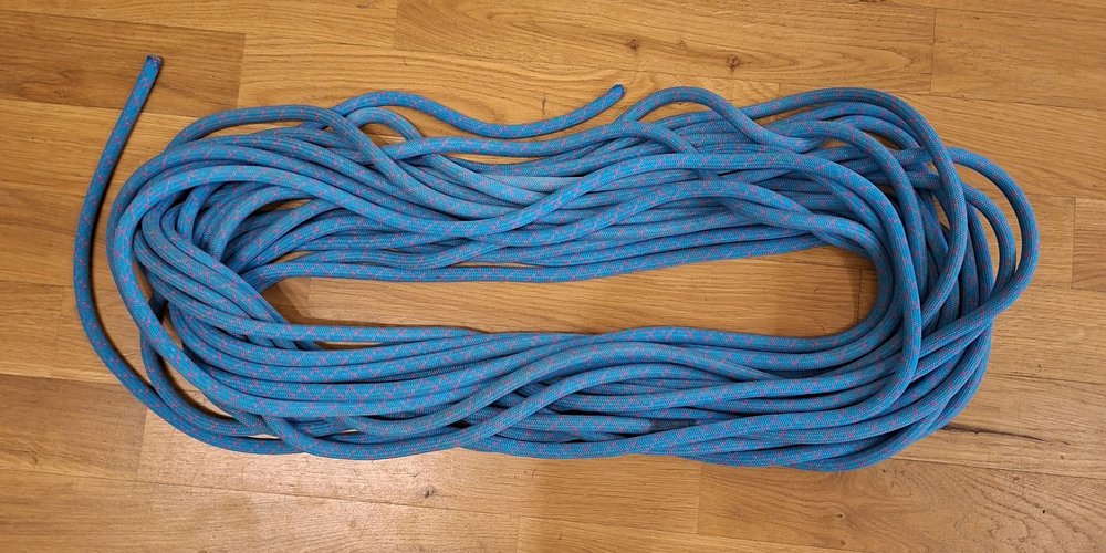 A blue climbing rope coiled into a neat oval of parallel circular loops on a wooden floor.