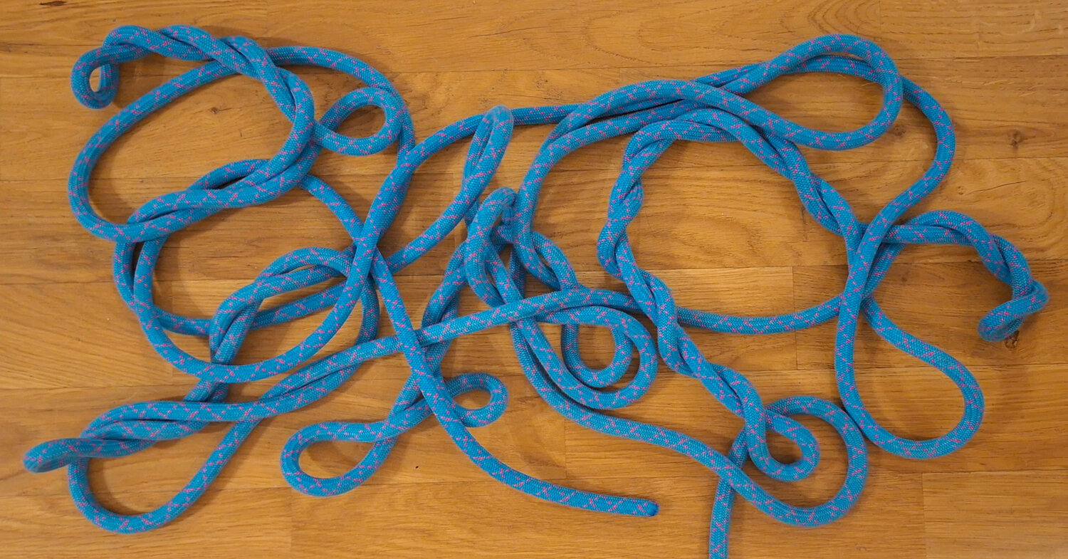 A blue climbing rope twisted into a tangle of loops on a wooden floor.